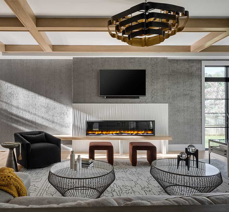 A wide photo showing a family room with 80” linear fireplace with custom surround of Porcelanosa® Oxo Line Blanco tile, white ceiling with natural wood beam coffered ceiling.
