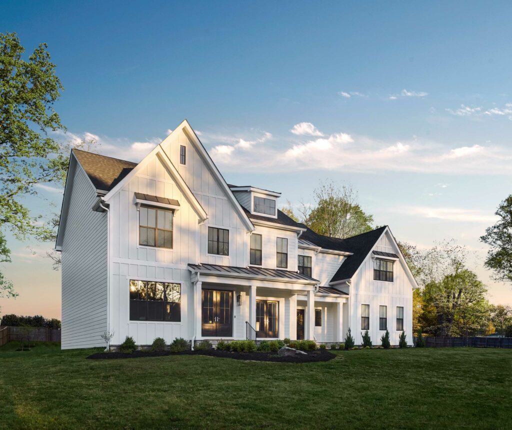 A modern farmhouse front exterior in white board and batten with two covered entrances and dark colored windows.