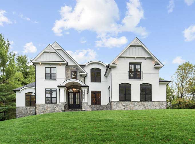 A transitional colonial elevation of white brick and grey stone with a unique curved roof portico, double reverse gable and other matching details.