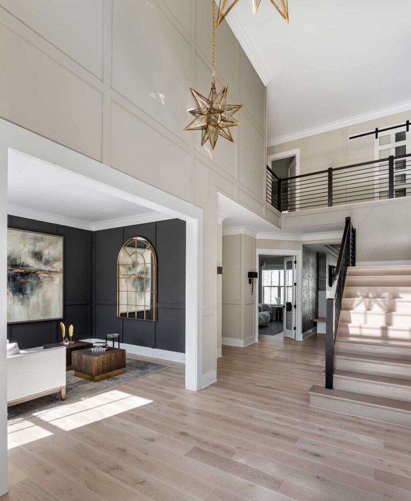 A tall photo showing a modern two-story foyer, dark paneled living room to the left, stairs to the right, white risers, natural stairs, iron rails