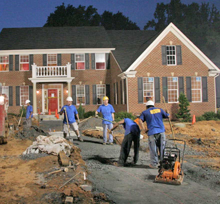 A crew works on the leadwalk to the home late at night with lights on the front yard