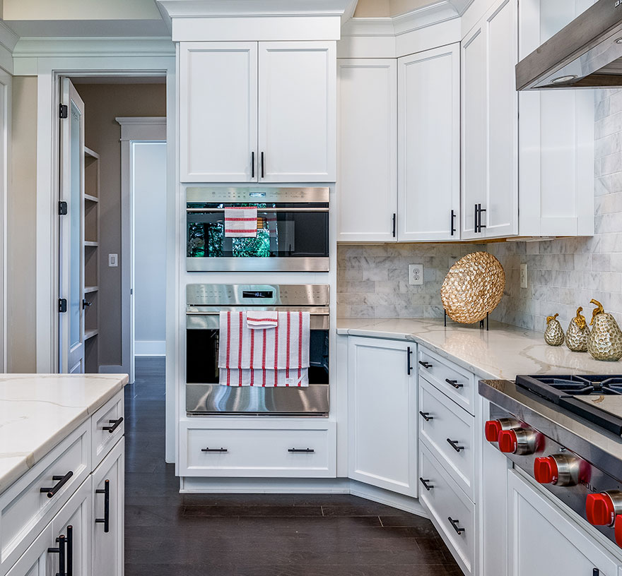 Kitchen detail showing double wall oven, white cabinets, quartz countertops and tile wall, modern hardware