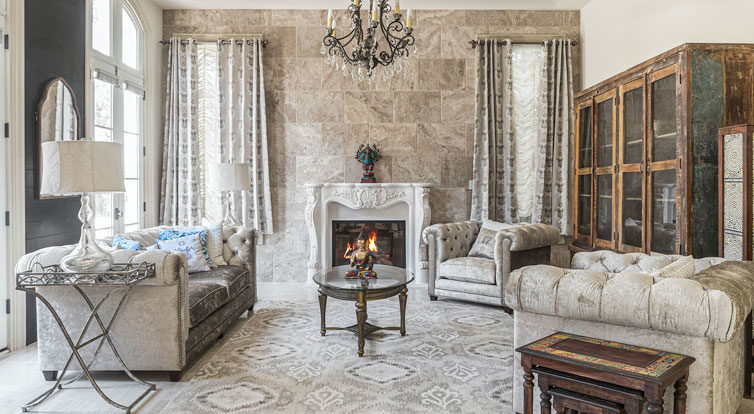 A luxurious living room with tile wall, custom fireplace surround, dark trimmed tray ceiling and tall windows.