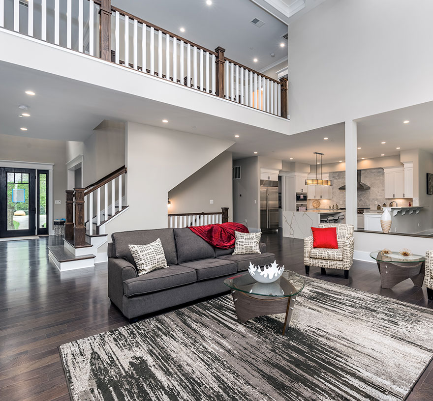 A two story family room space open to above and the kitchen beyond, stained rails and white posts on stairs and overlook