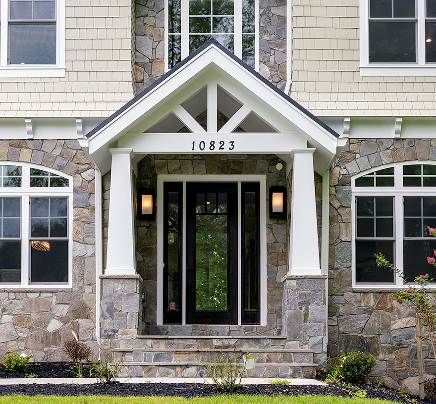 A front porch in a craftsman style with stone and hardie shingle, dark front door, flagstone stoop and stairs