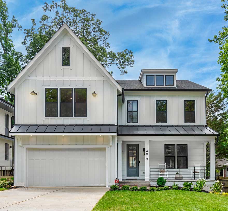 A narrow modern farmhouse style front exterior, white board and batten, black windows, black horizontal iron rails and black metal porch and garage roofs.