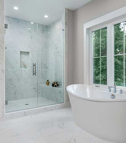 The master bath of the Wilmett model home with frameless shower with floor to ceiling tile, tiled bench and free standing tub in the foreground.