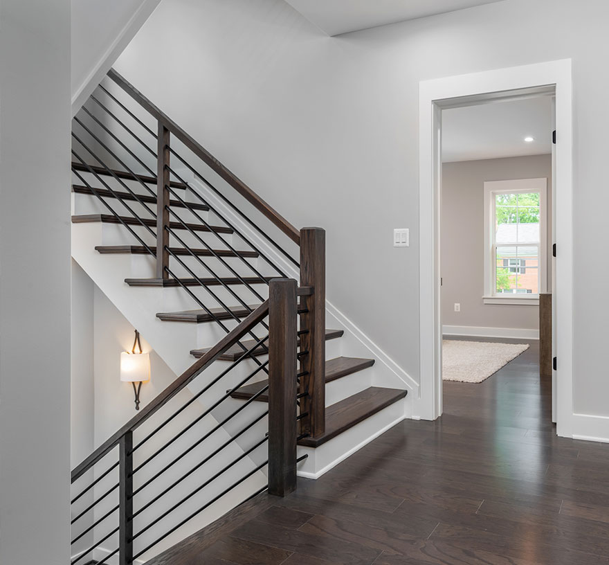 A modern farmhouse style staircase with white painted risers and stained wood steps and posts, black iron horizontal rails.