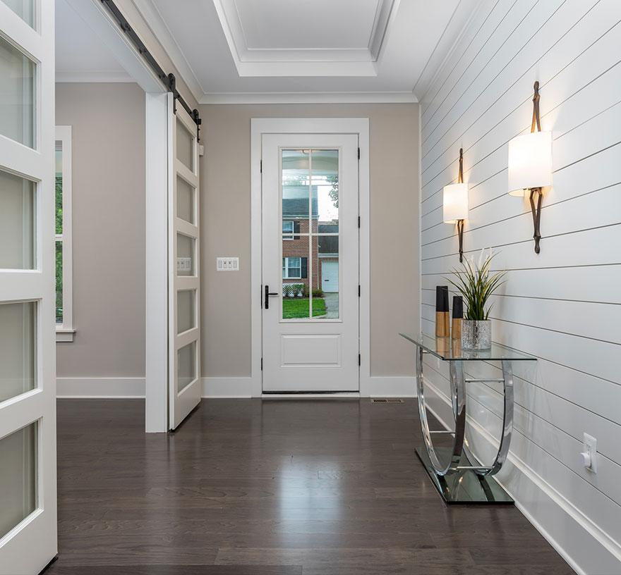 The entry foyer of a modern farmhouse style home a shiplap wall deep tray ceiling and glass barn doors to the study.