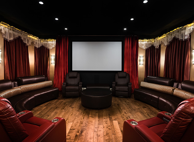 A home movie theater with red leather recliners, benches, hardwood flooring and red curtains.