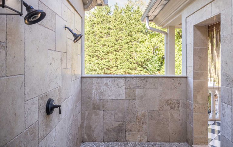 A private outdoor shower with tile wall, dual shower heads, chest hall exterior wall and entrance to private balcony.
