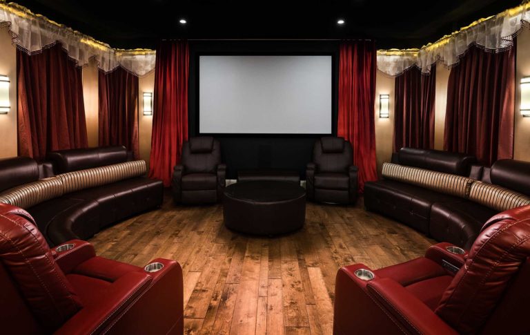 A home movie theater with red leather recliners, dark leather benches, red curtains around the screen and hardwood flooring.