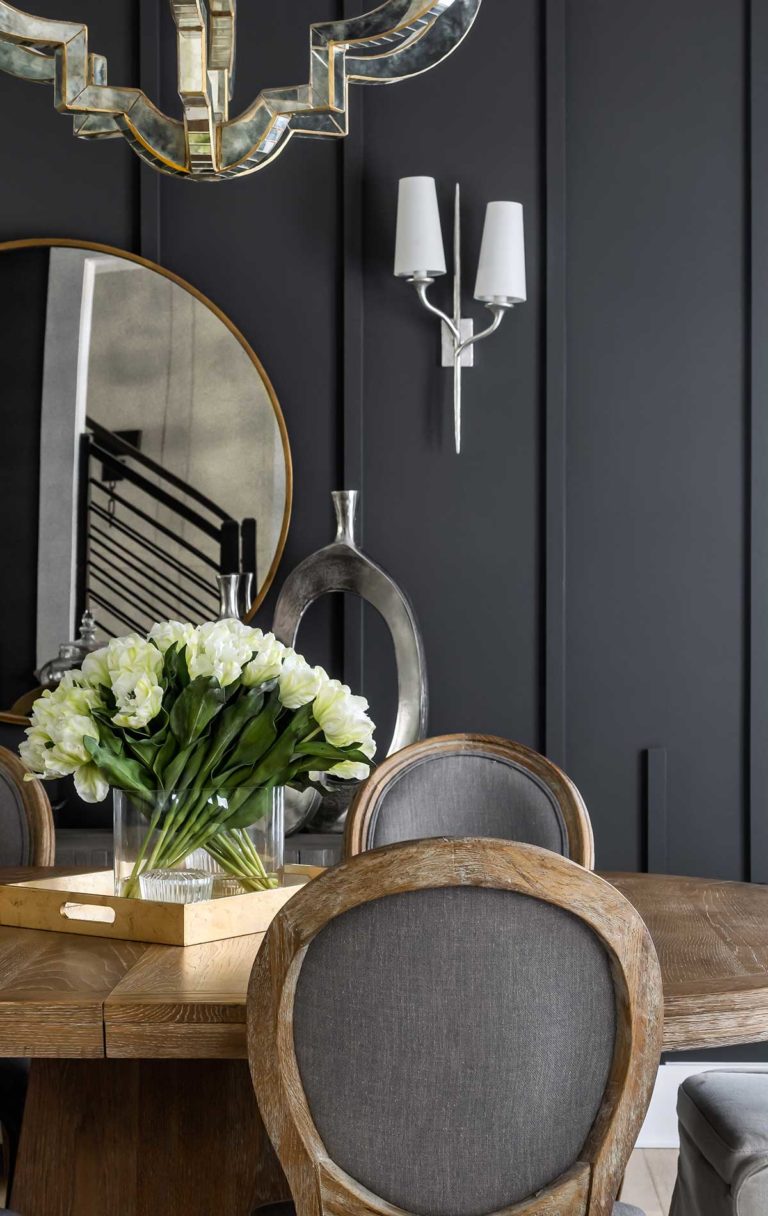 Dining room table and chair in the foreground, dark paneled wall with mirror reflecting staircase