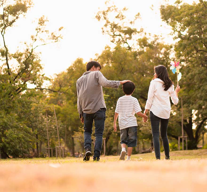 A stock photo showing parents and child walking in the park playfully.