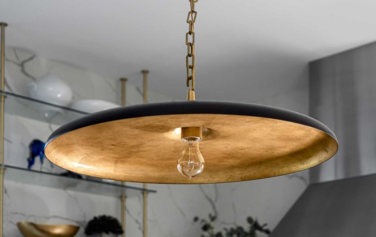 A close up photo of a circular lamp, dark on top, brass underneath, suspended from the ceiling.