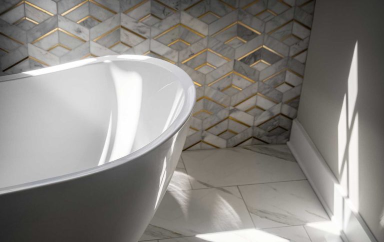 A partial image of a free standing tub in front of an accent wall of Lavaliere Alluring white/brass tile.