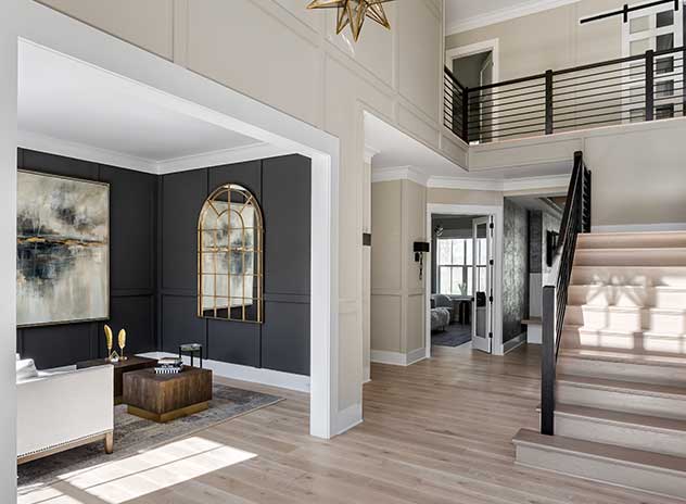 A tall photo showing a modern two-story foyer, dark paneled living room to the left, stairs to the right, white risers, natural stairs, iron rails