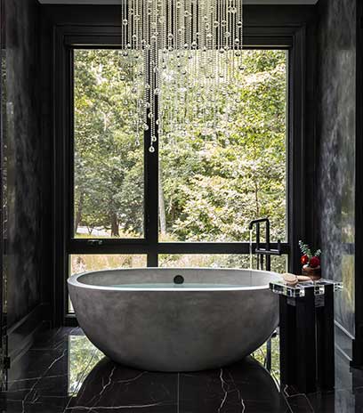 A stunning Owner's Bath with elegant chandelier, free standing tub filler, and view of the wooded surroundings.