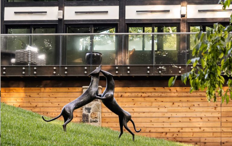 Looking up at the rear of deck from the backyard, art sculpture of playing dogs in the yard in the foreground.
