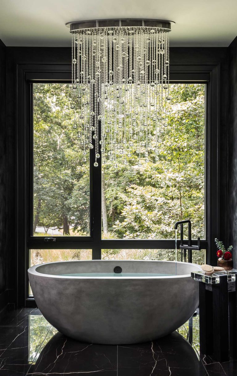 A stunning Owner's Bath with elegant chandelier, free standing tub filler, and view of the wooded surroundings.
