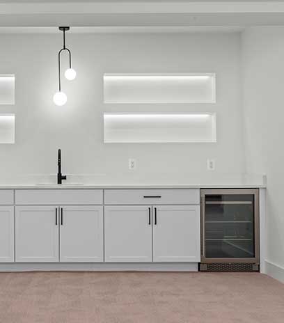 A wet bar detail showing built-in shelving, wine fridge fixture, white cabinets and a contemporary light.