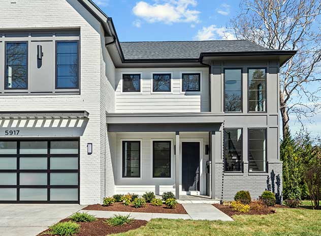 Photo of a transitional modern custom home elevation with white siding, grey patterned panels, industrial portico and exposed staircase.