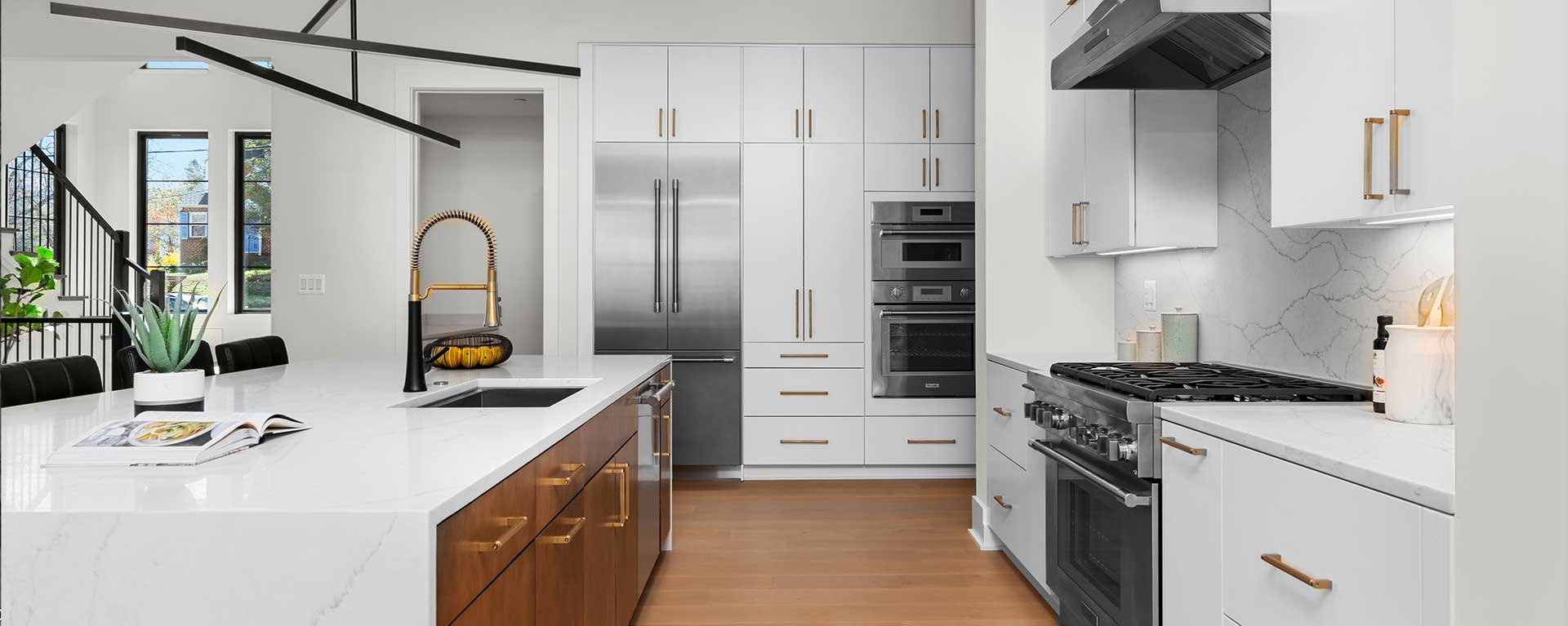 A contemporary Kitchen with custom white cabinets with gold hardware, white quartz waterfall island with stained cabinet underneath, gourmet range, built-in appliances and quartz backsplash.
