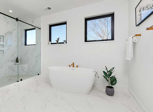 An owner's suite bath detail showing a free standing tub and frameless glass shower, square black windows on the far wall