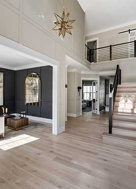 A tall photo showing a modern two-story foyer, dark paneled living room to the left, stairs to the right, white risers, natural stairs, iron rails