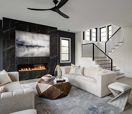 An oversized linear fireplace surround of dark Daltile Marble Attaché with dark windows, neutral colored couches and brown coffee table in the foreground