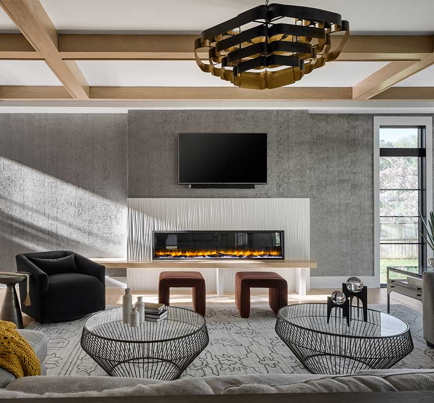A family room with 80” linear fireplace with custom surround of Porcelanosa® Oxo Line Blanco tile, white ceiling with natural wood beam coffered ceiling.