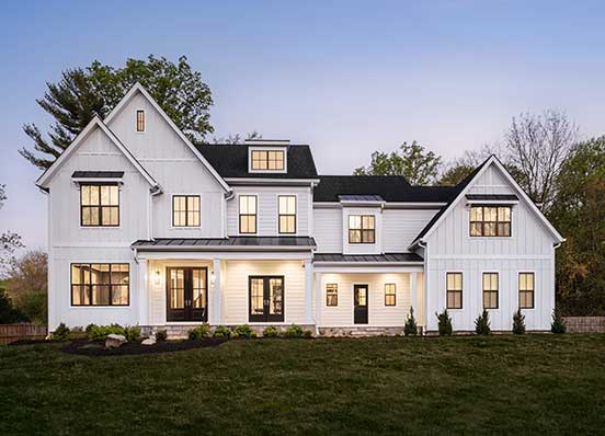 A modern farmhouse front exterior in white board and batten with two covered entrances and dark colored windows.