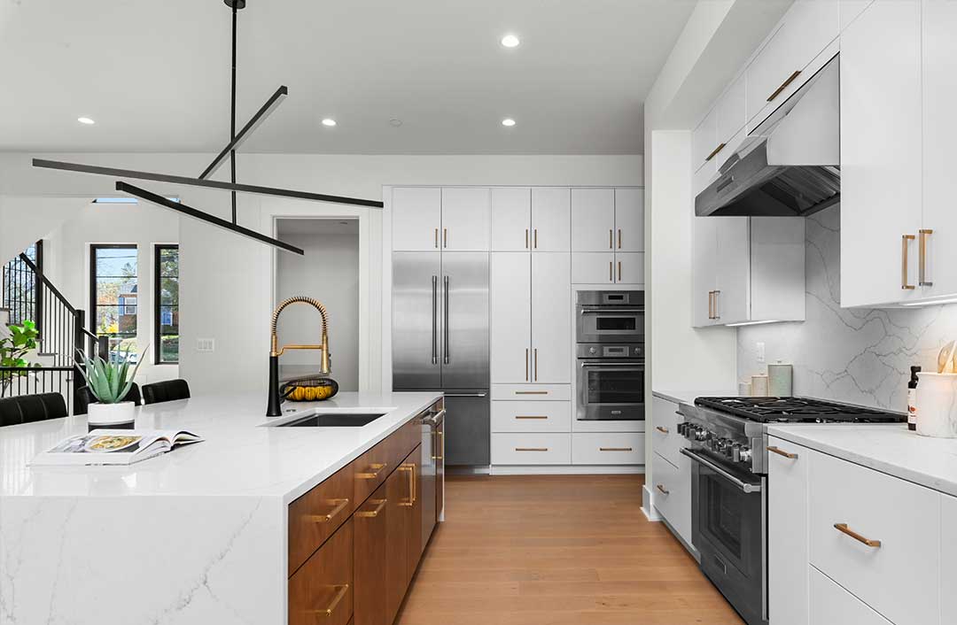 A white quartz waterfall island with contrasting natural stained cabinets underneath, gourmet range to the right, two story foyer in the distance on the left.