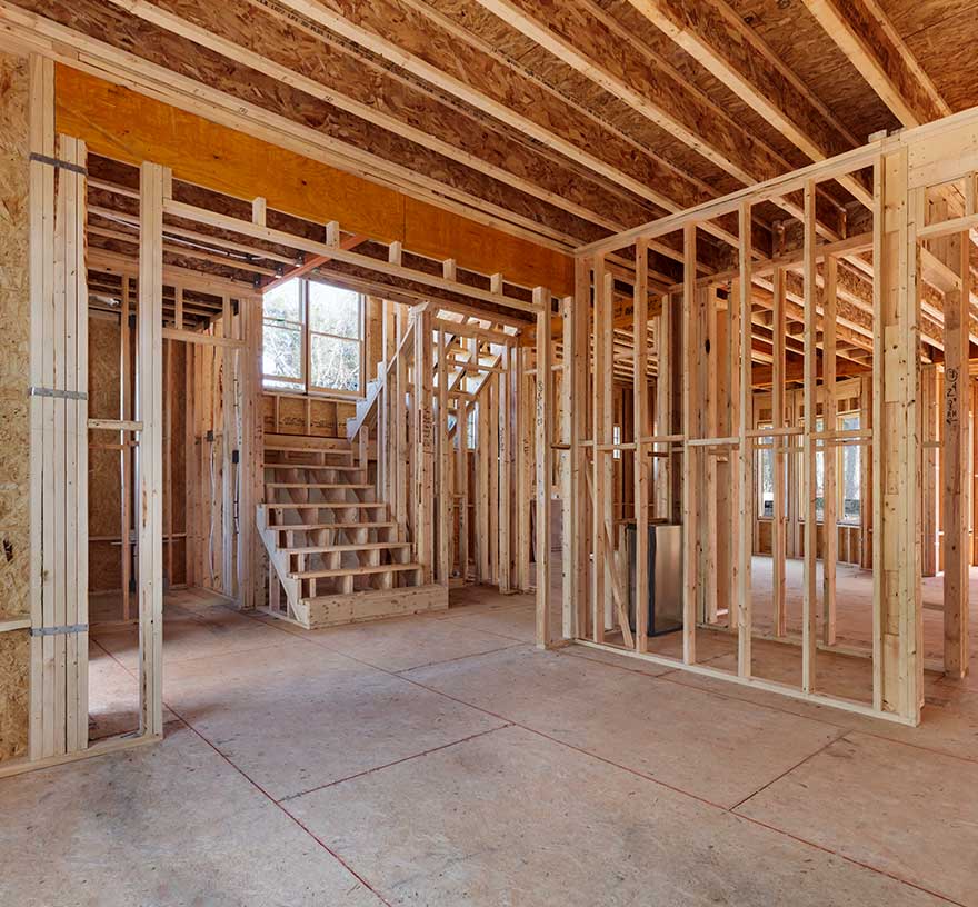 A photo of a house under construction in framing, looking towards the stairs from the main level