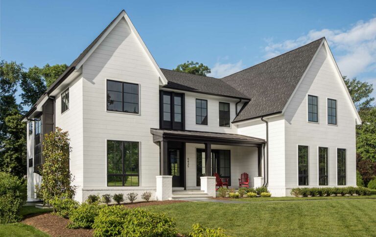 A custom modern farmhouse exterior with black and white detailing on a green lawn with a blue sky.