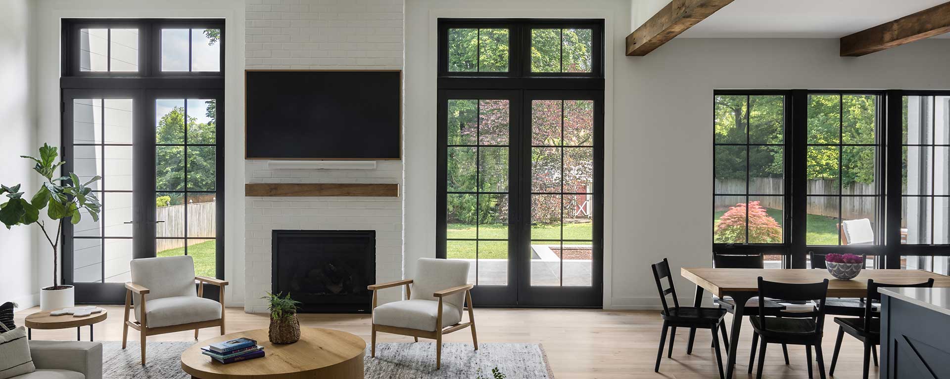 A custom modern farmhouse family room with natural exposed rough beams, two sets of doors to the patio, and kitchen island visible to the right