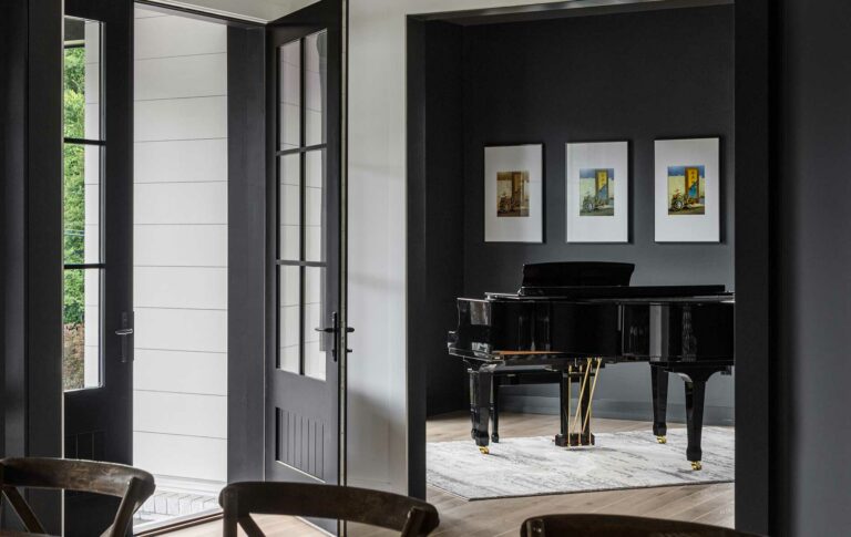 A front door opens into the foyer with a grand piano visible against a dark accent wall adorned with artwork