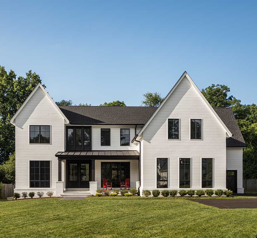 A custom modern farmhouse exterior with black and white detailing on a green lawn with a blue sky.
