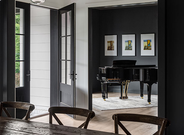 A front door opens into the foyer with a grand piano visible against a dark accent wall adorned with artwork