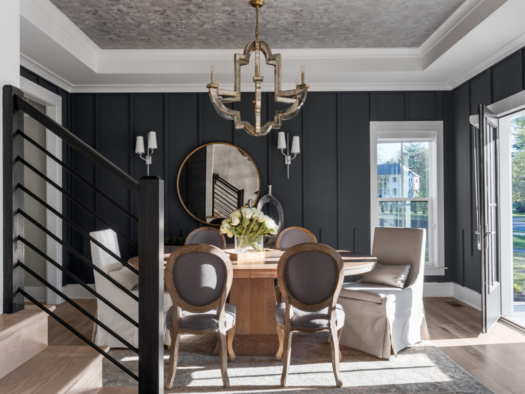 Dining room with silver wall paper in tray ceiling, dark paneled walls, horizontal iron stair rails in foreground, door open to outside