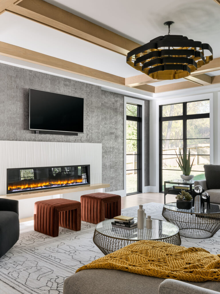 A vertical shot of the A family room with 80” linear fireplace with custom surround of Porcelanosa® Family Room showing Oxo Line Blanco tile, white ceiling with natural wood beam coffered ceiling.