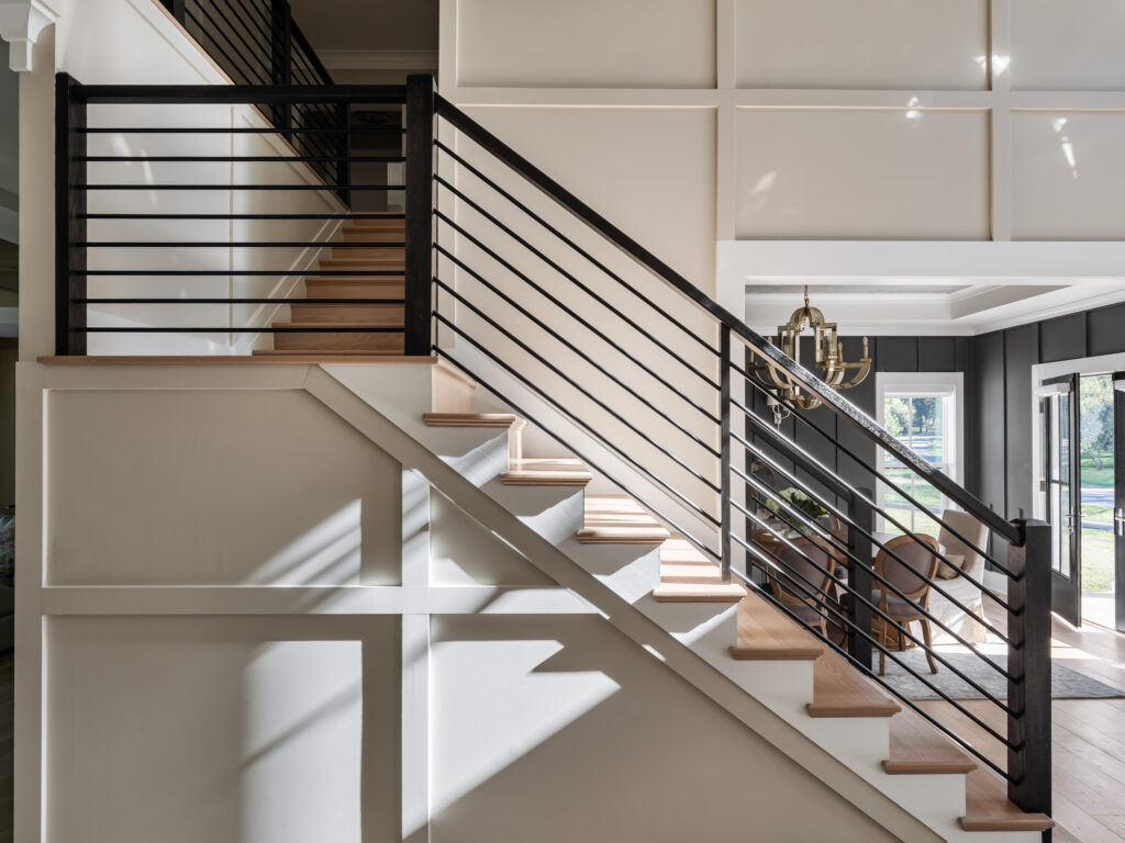 A detail image of the foyer showing the shadow boxes on the front of the staircase, horizontal iron rails, white painted risers and stained wood treads.