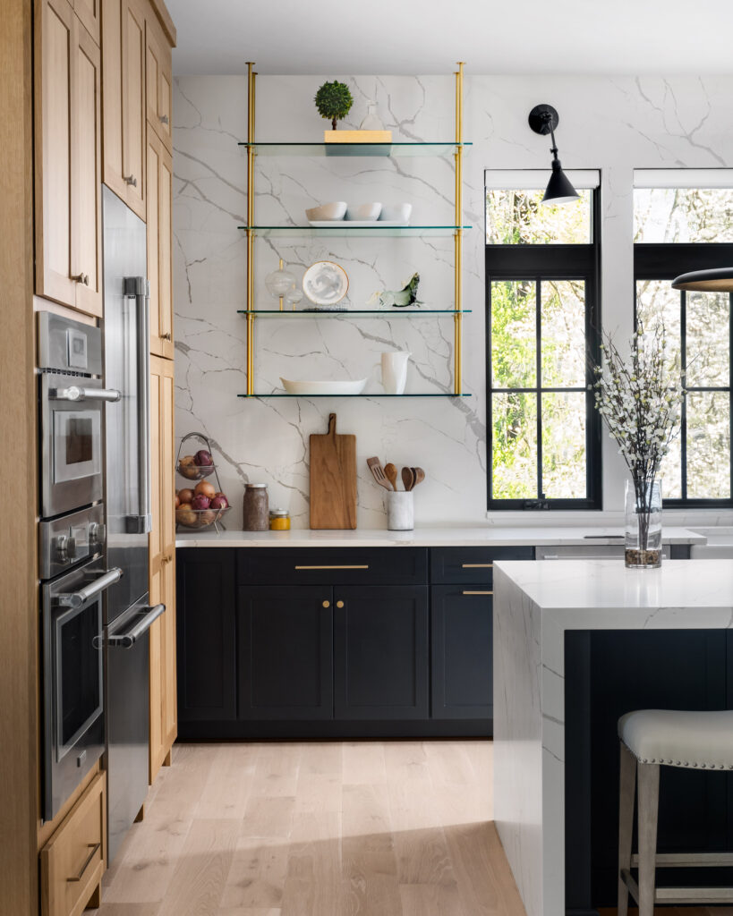 quartz waterfall island in the foreground, quartz accent wall with floating brass shelves and dark windows behind