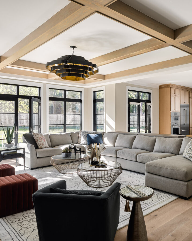 A cat stands on the table in the center of a luxury family room with large glass windows and doors to the backyard.