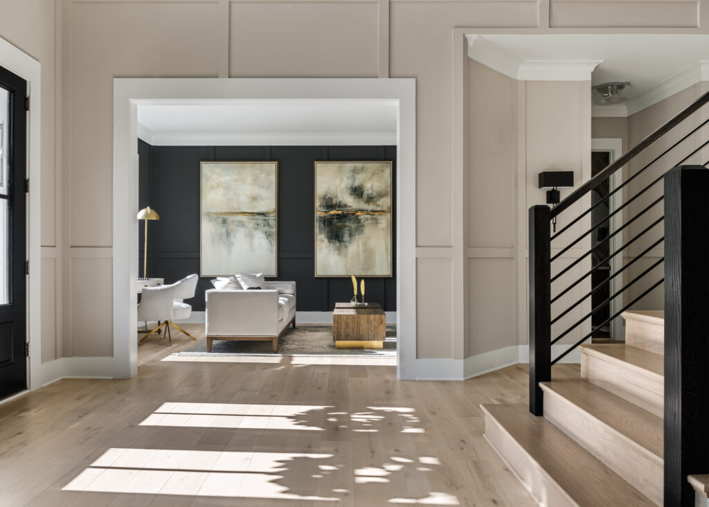 A looking into a  dark paneled living room, neutral furniture in the center, from the foyer, stairs in the foreground to the right.