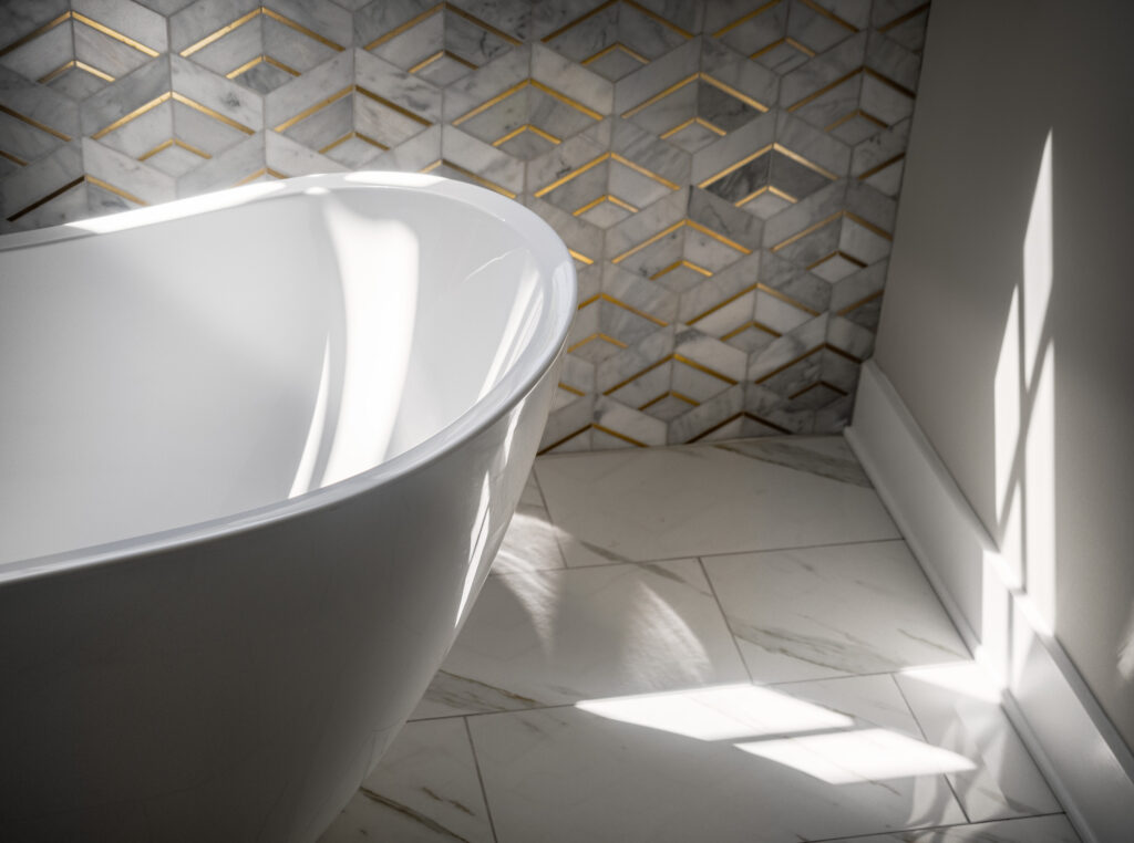 A partial image of a free standing tub in front of an accent wall of Lavaliere Alluring white/brass tile.