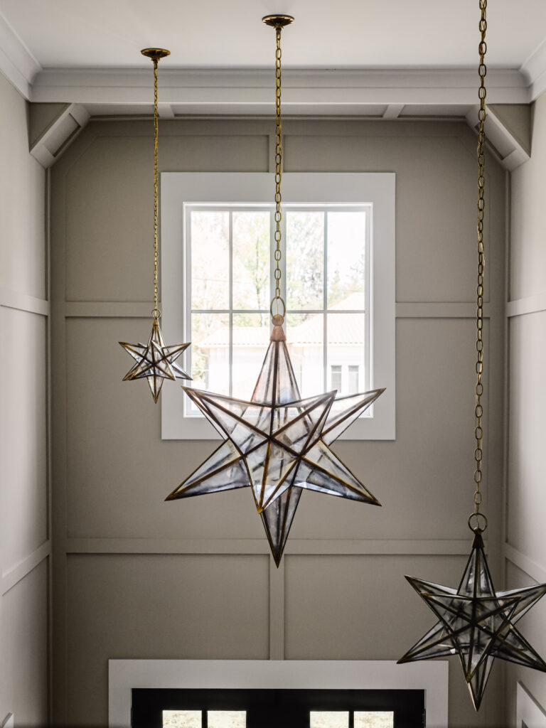 A photo showing ornate star shaped chandeliers in front of a large window atop a two story foyer.