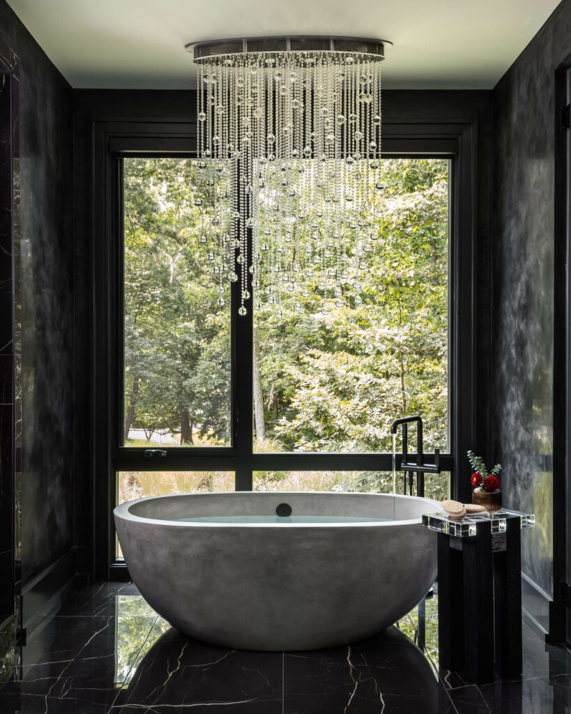 A stunning Owner's Bath with elegant chandelier, free standing tub filler, and view of the wooded surroundings.