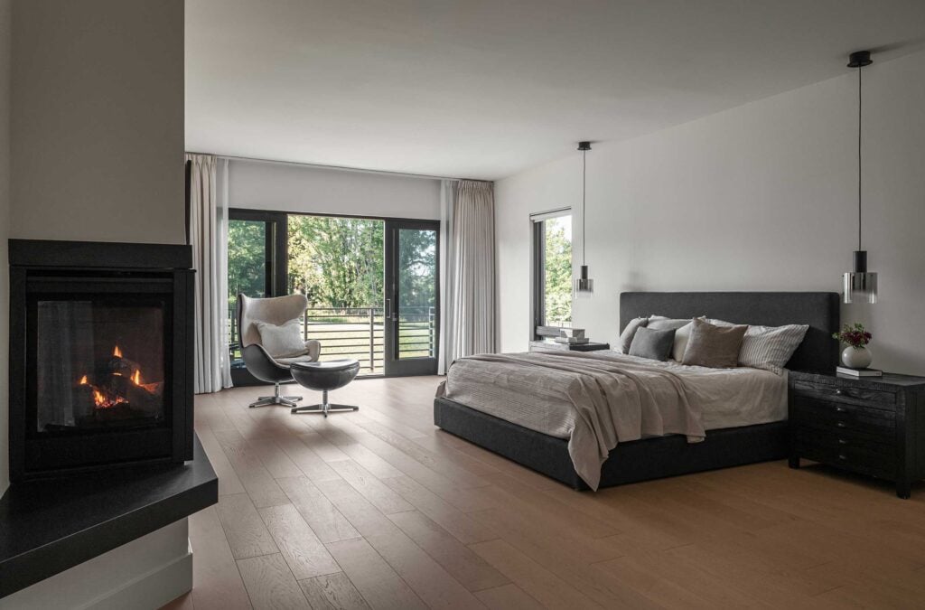 An Owner's Suite bedroom with double sided fireplace in the foreground and balcony with horizontal rails on the far wall.