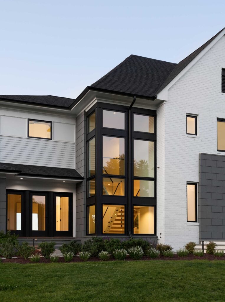 A detail shot showing a two story exposed stair case behind dark framed tall modern windows on white brick house with custom paneling.
